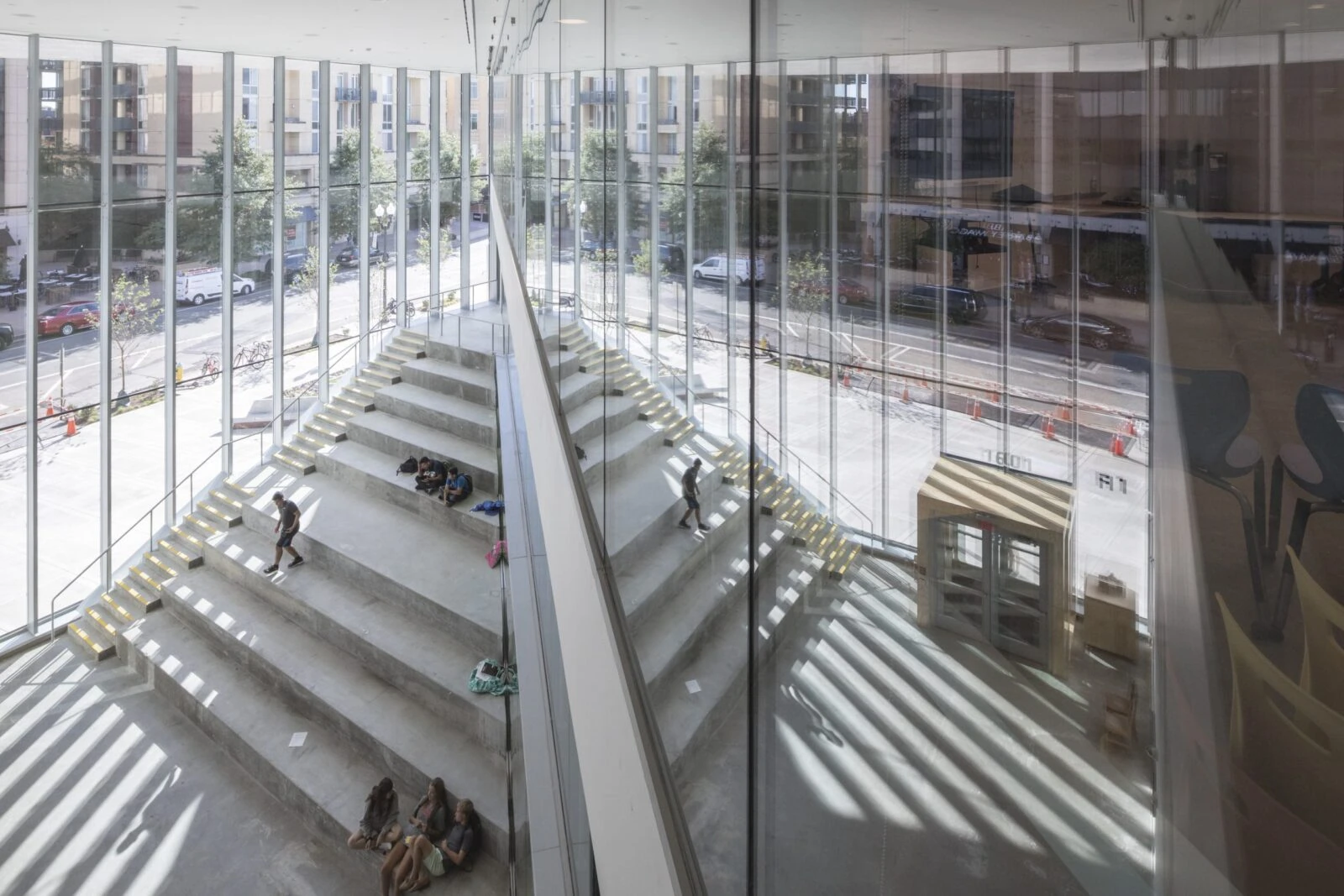 Modern glass staircase and escalator in a bright, spacious building interior.