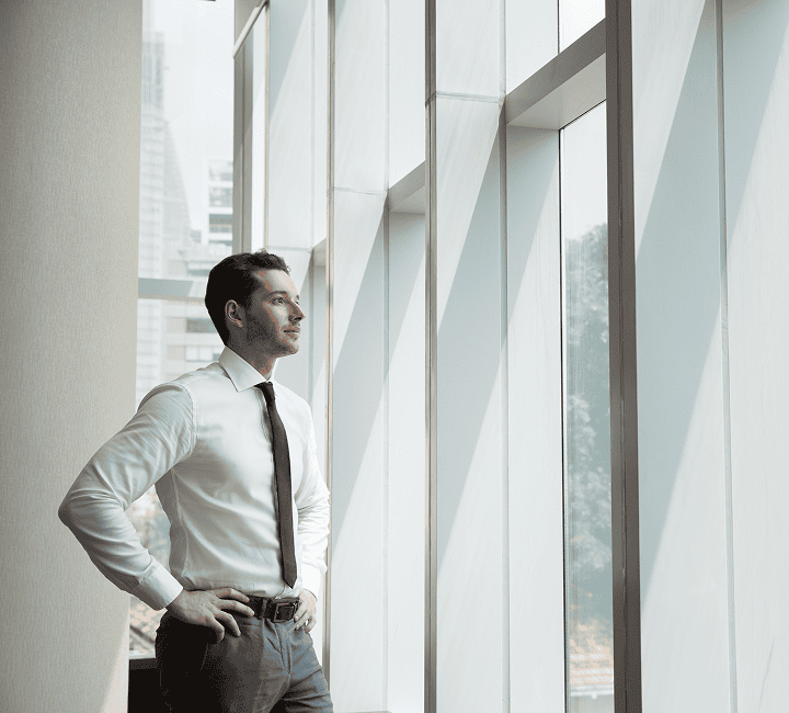 Businessman gazing out of office window with city view.