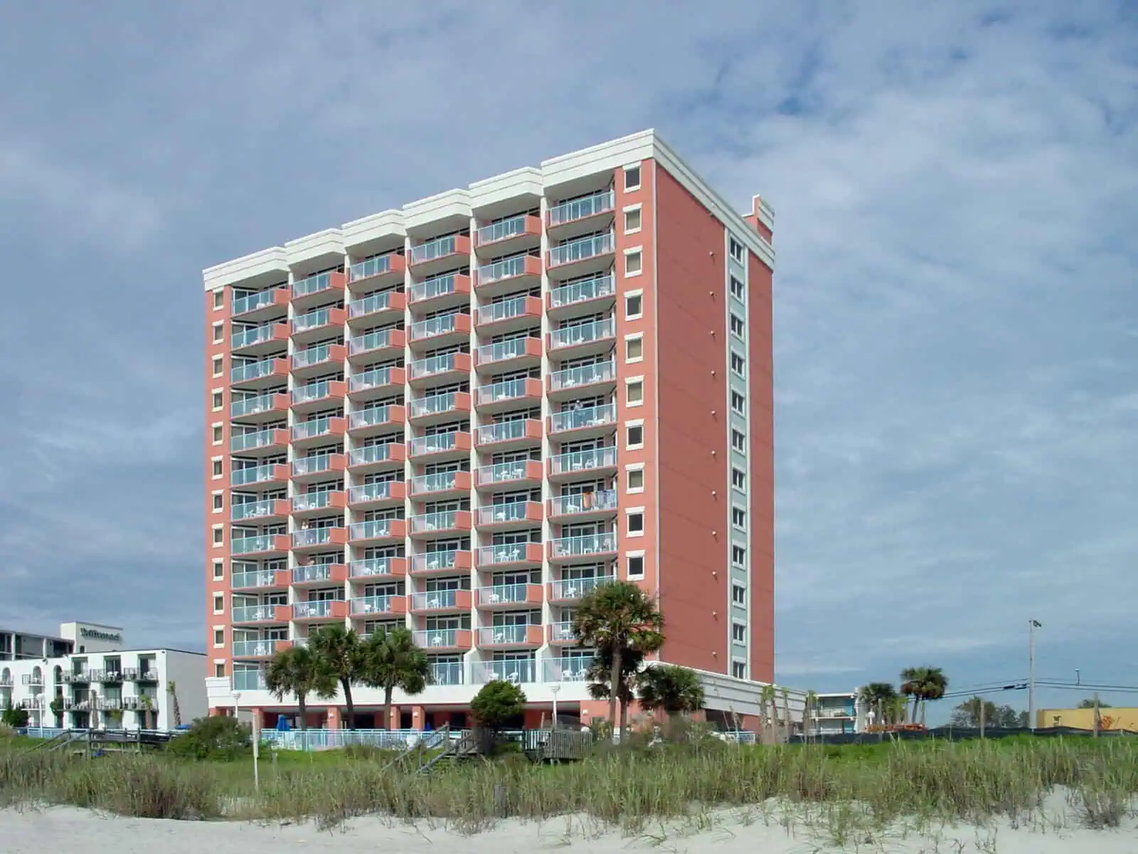 A modern multi-story building with balconies and palm trees in front.