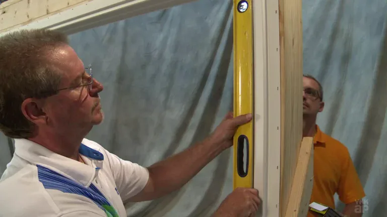 A man using a level to install a window frame in a construction site.
