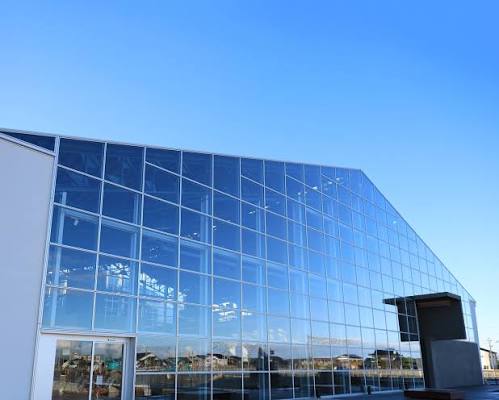 Modern glass building reflecting the blue sky, part of YKK's innovative history.